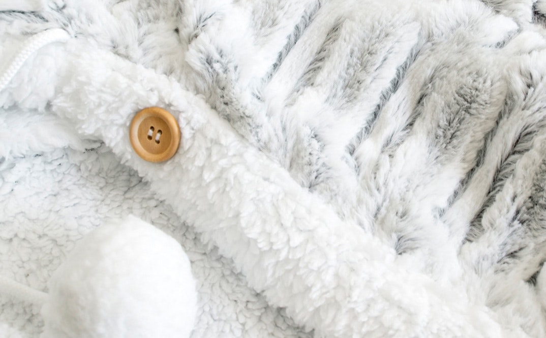 Girl sitting on a couch with the ardor hooded faux fur blanket