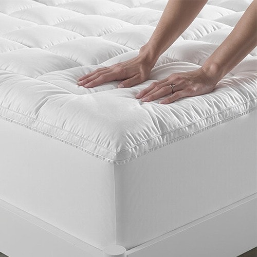 A person is gently touching the top of a mattress, assessing its softness and comfort.